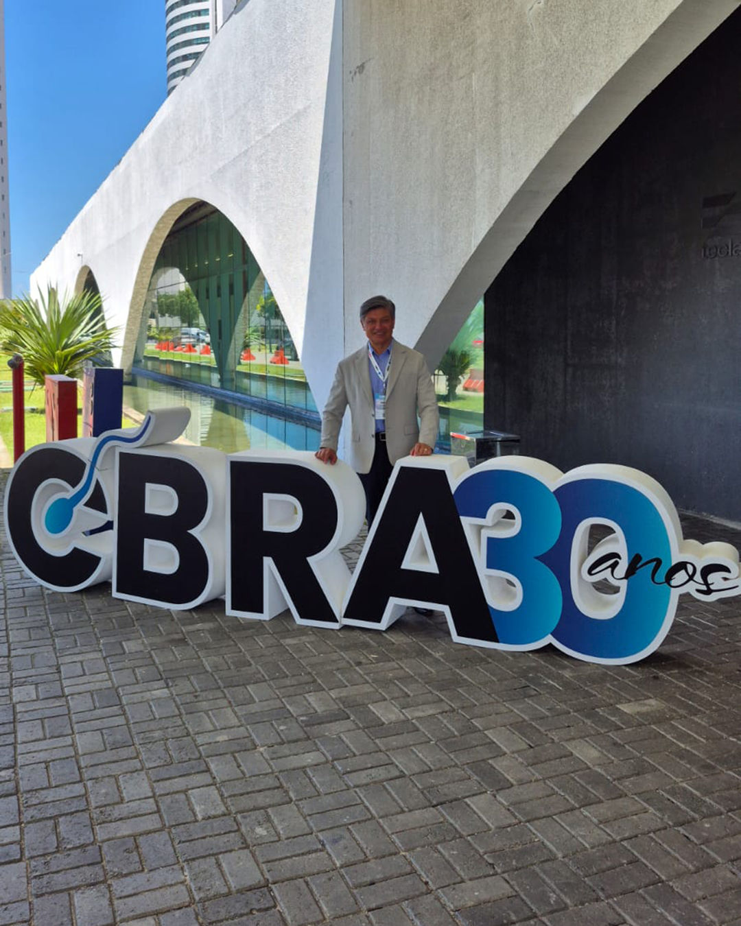 O Dr. Carlos Portocarrero ao lado do letreiro "CBRA 30 anos", no 30º Congresso Brasileiro de Reprodução Assistida, em Recife.